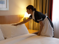 Chamber maid working in hotel bedroom.